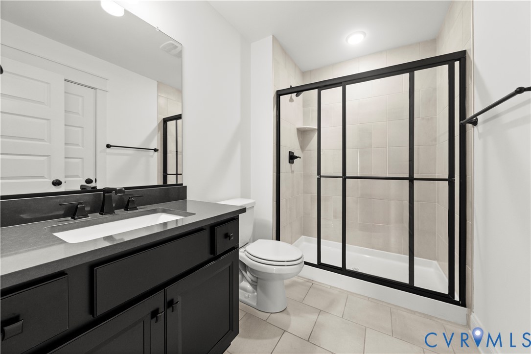Bathroom featuring a dark-finish vanity with a rectangular undermount sink, quartz countertop, walk-in shower with matte black sliding doors, and large-format tile flooring