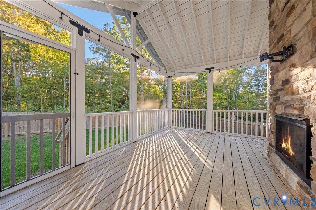Screened porch featuring a natural wood deck, stone-surround fireplace, vaulted ceiling, and white railing