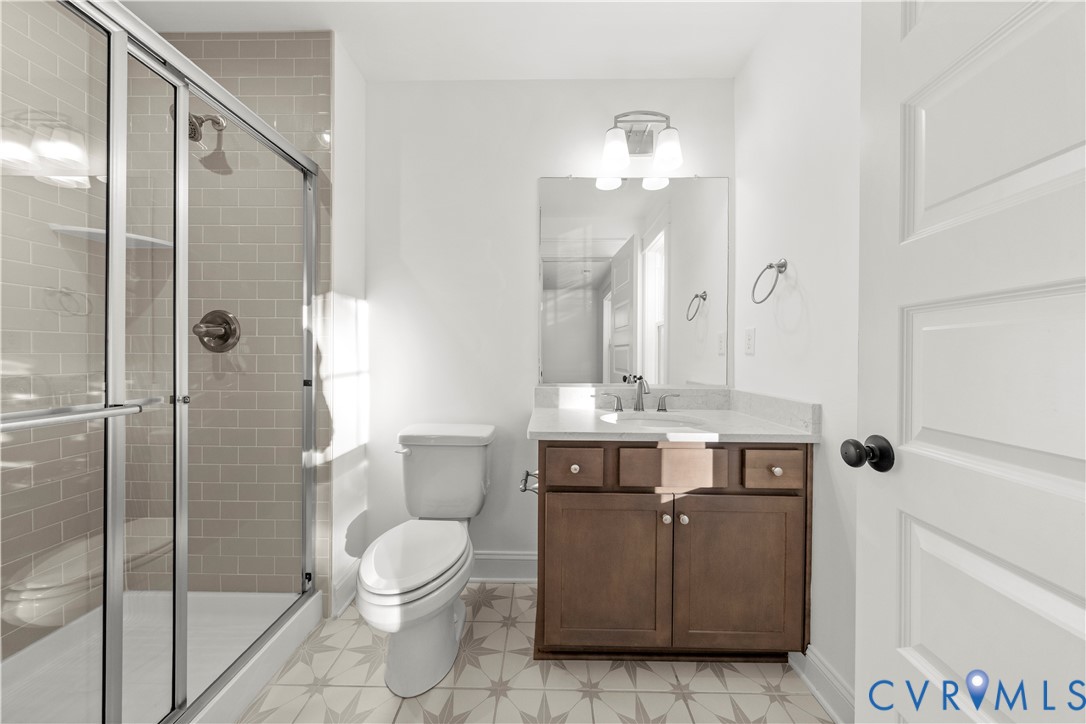 Bathroom featuring a glass-enclosed shower with subway tile surround, vanity with stone-finish countertop, patterned tile flooring, and integrated wall-mounted lighting