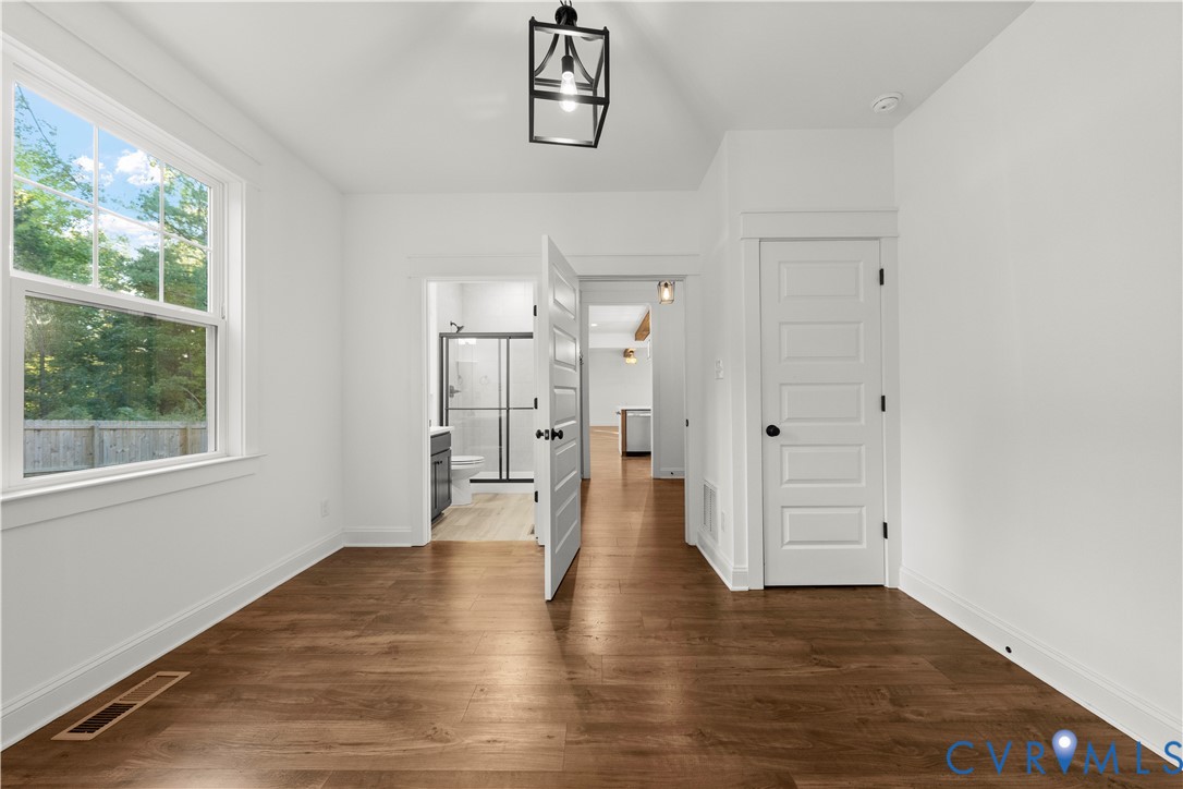 Vaulted ceiling with a geometric pendant light, wood-finish flooring, and single-hung window featuring a grid pattern
