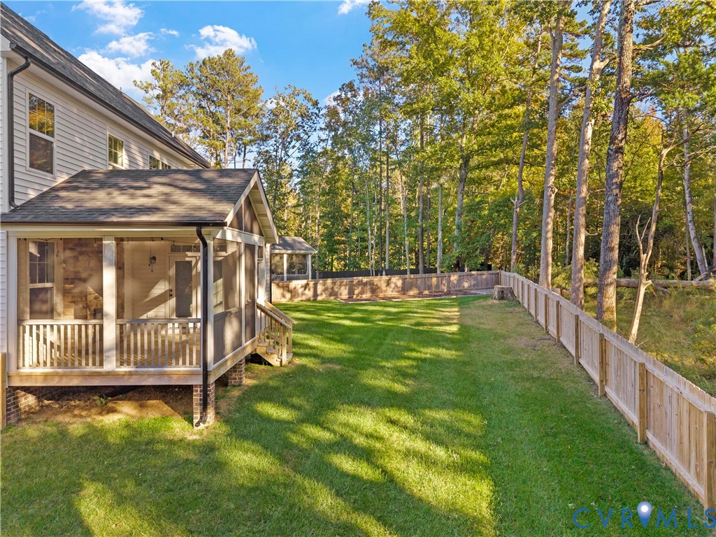 Screened porch featuring a shingle roof and brick foundation piers, paired with a fenced backyard, manicured lawn, and mature trees