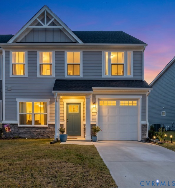 Two-story exterior featuring gray lap siding, stone veneer base, a gabled roofline with decorative trim, and a concrete driveway