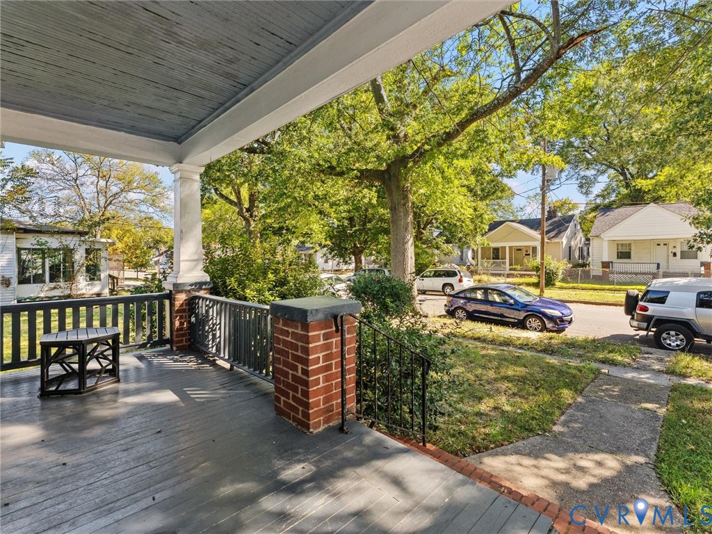 Covered front porch featuring painted wood decking, a solid column, and brick masonry pillars with black wrought-iron railings
