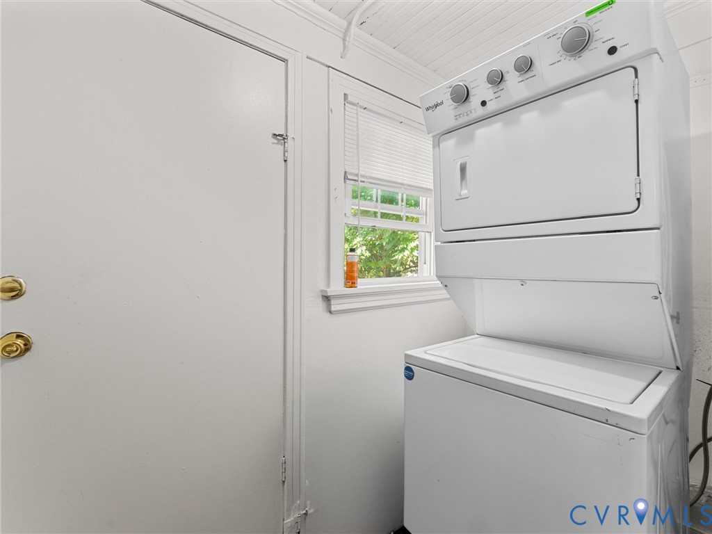 Stacked laundry unit, window with horizontal blinds, beadboard ceiling, and solid-core door with metallic hardware