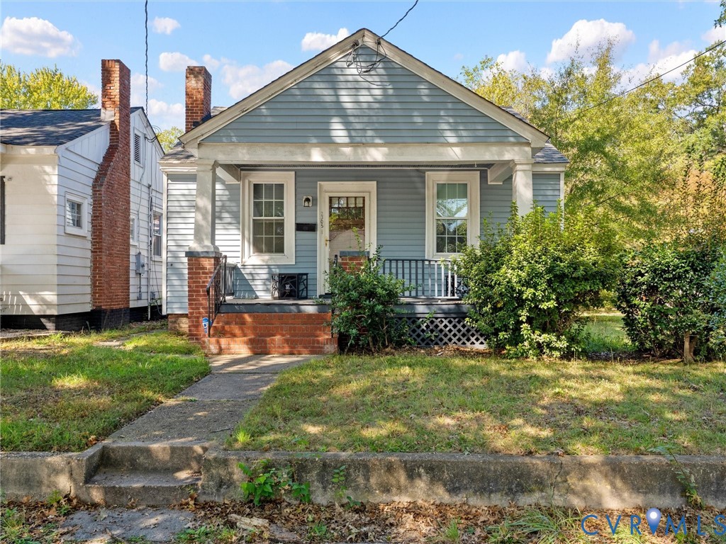Blue horizontal siding exterior featuring a front-facing gable roof, a covered porch with tapered columns, a brick foundation, and multi-pane windows Blue horizontal siding exterior featuring a front-facing gable roof, a covered porch with tapered columns, a brick foundation, and multi-pane windows