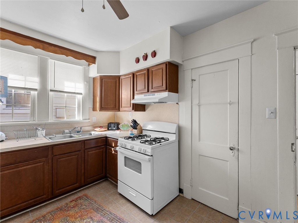 Kitchen featuring stained wood cabinetry, white gas range with integrated vent hood, stainless steel dual-basin sink, and multi-pane windows