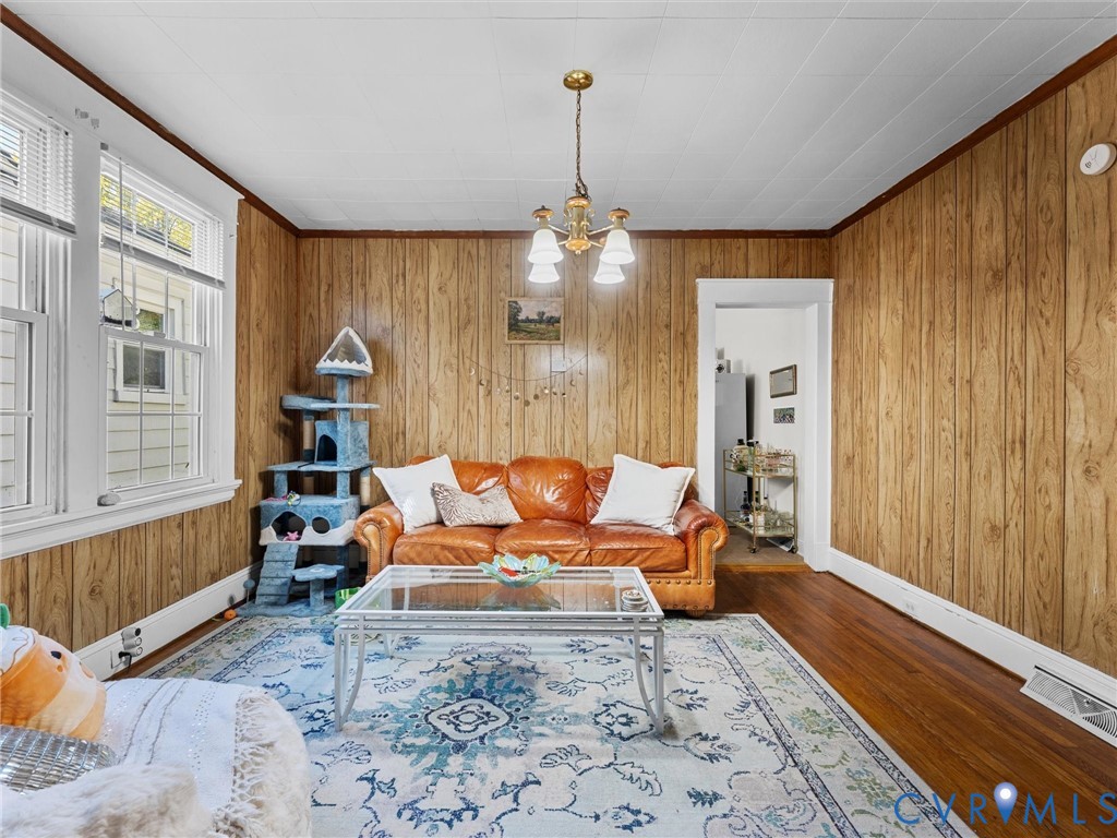 Interior room featuring wood-paneled walls, hardwood flooring, multi-pane windows, and a classic four-light ceiling chandelier