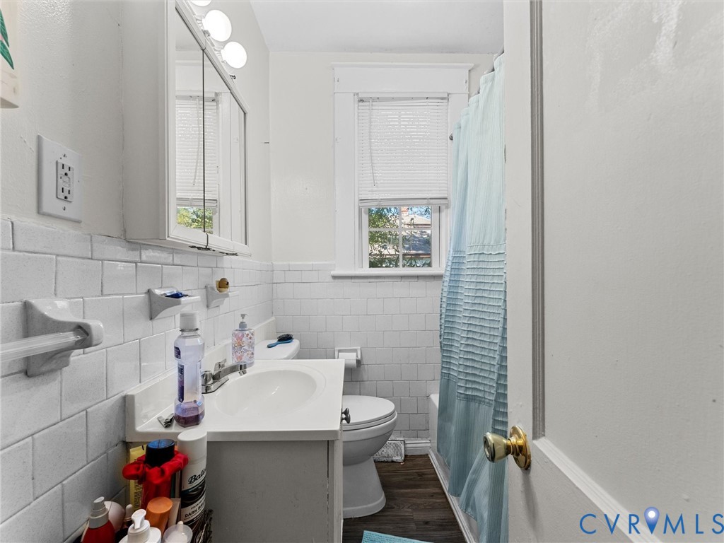 Bathroom featuring white subway tile wall cladding, wood-finish flooring, a white vanity with an integrated sink, a mirrored medicine cabinet, and a window with trim detail