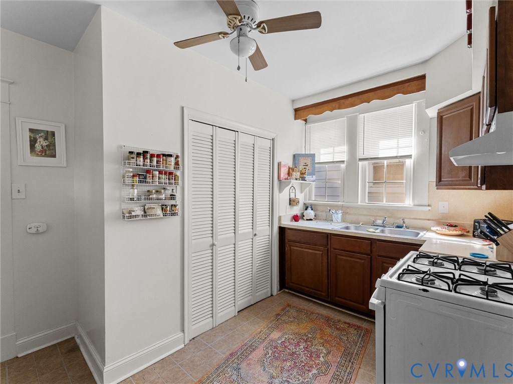 Kitchen featuring wood cabinetry, stainless steel double-basin sink, gas range, louvered-door pantry, and ceiling fan
