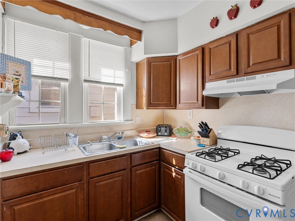 Kitchen featuring wood cabinetry, solid-surface countertops, a double-basin stainless steel sink, and large windows with blinds