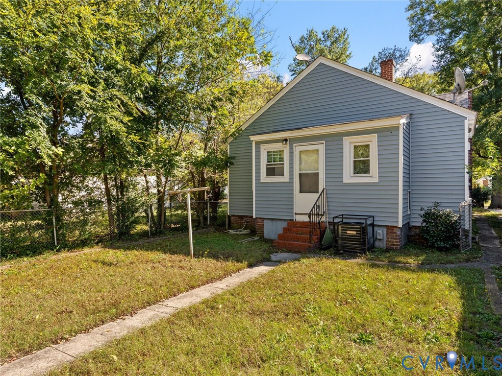 Rear exterior featuring blue horizontal siding, brick foundation elements, concrete walkway, and chain-link fencing