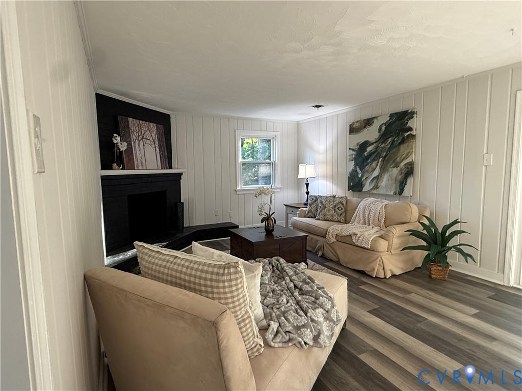 Vertical paneling, wood-finish flooring, and a fireplace with a black-finish mantel and hearth