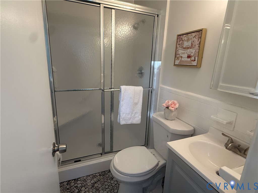 Bathroom featuring a walk-in shower with a sliding glass door, a vanity with an integrated sink, a solid-surface countertop, and penny-round tile flooring