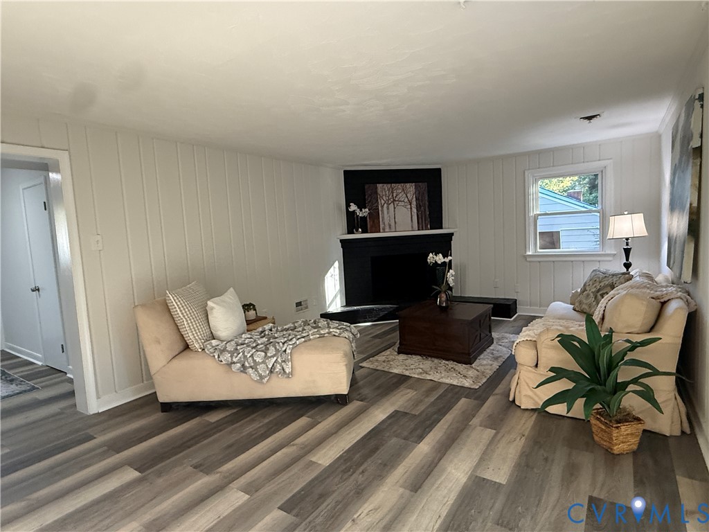 Living area featuring vertical paneled walls, wood-finish flooring, and a corner fireplace with a black surround and mantle
