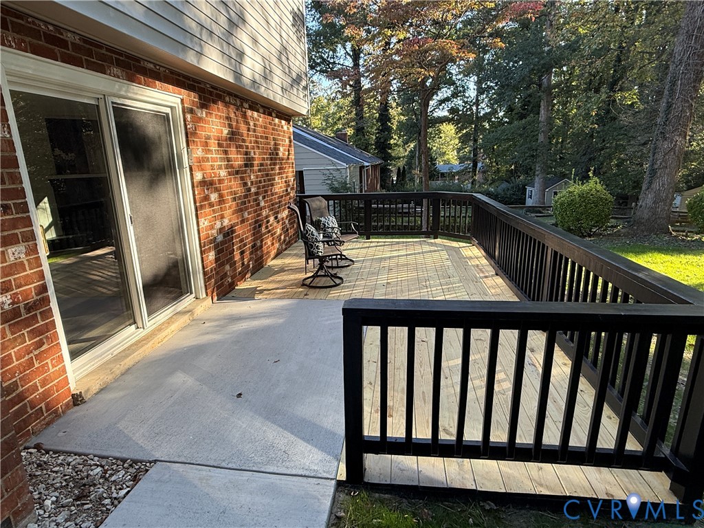 Multi-level exterior space featuring a concrete patio, wood-decking platform, black railing, brick siding, and a sliding glass door