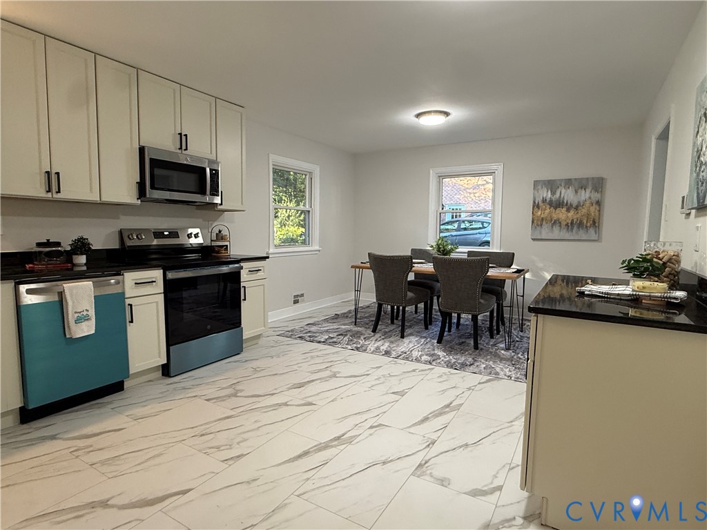 Kitchen featuring white cabinetry, dark countertops, integrated stainless steel appliances, and large-format tile flooring