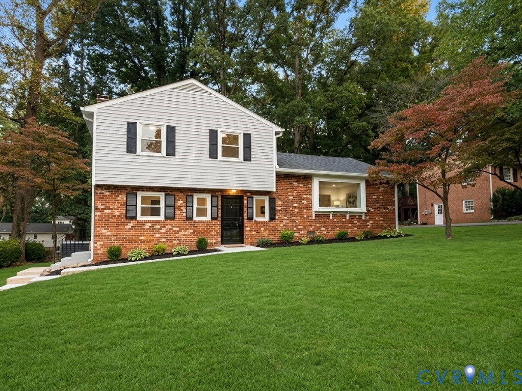 Two-story residence featuring a combination brick and light-toned horizontal siding exterior, contrast window shutters, a large picture window, and a landscaped lawn with mature trees