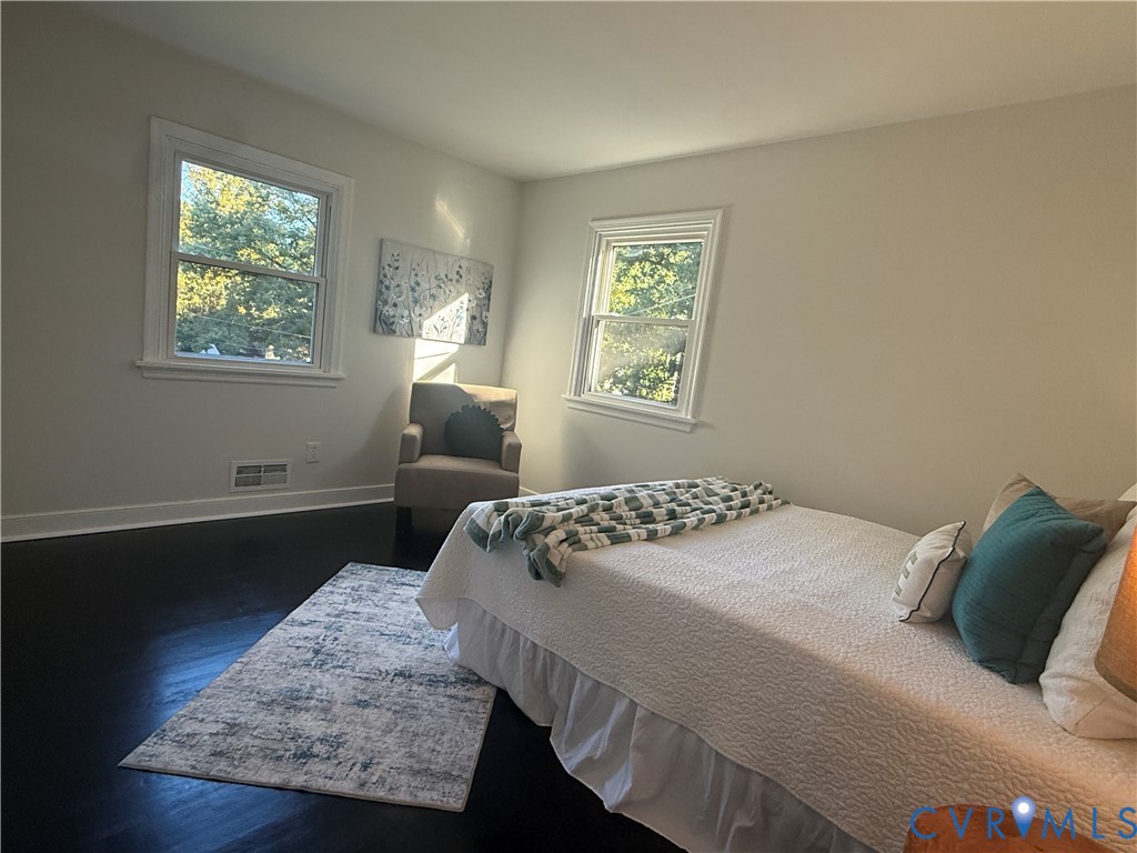 Room featuring dark wood-finish flooring, neutral wall paint, and two double-hung windows with white casing