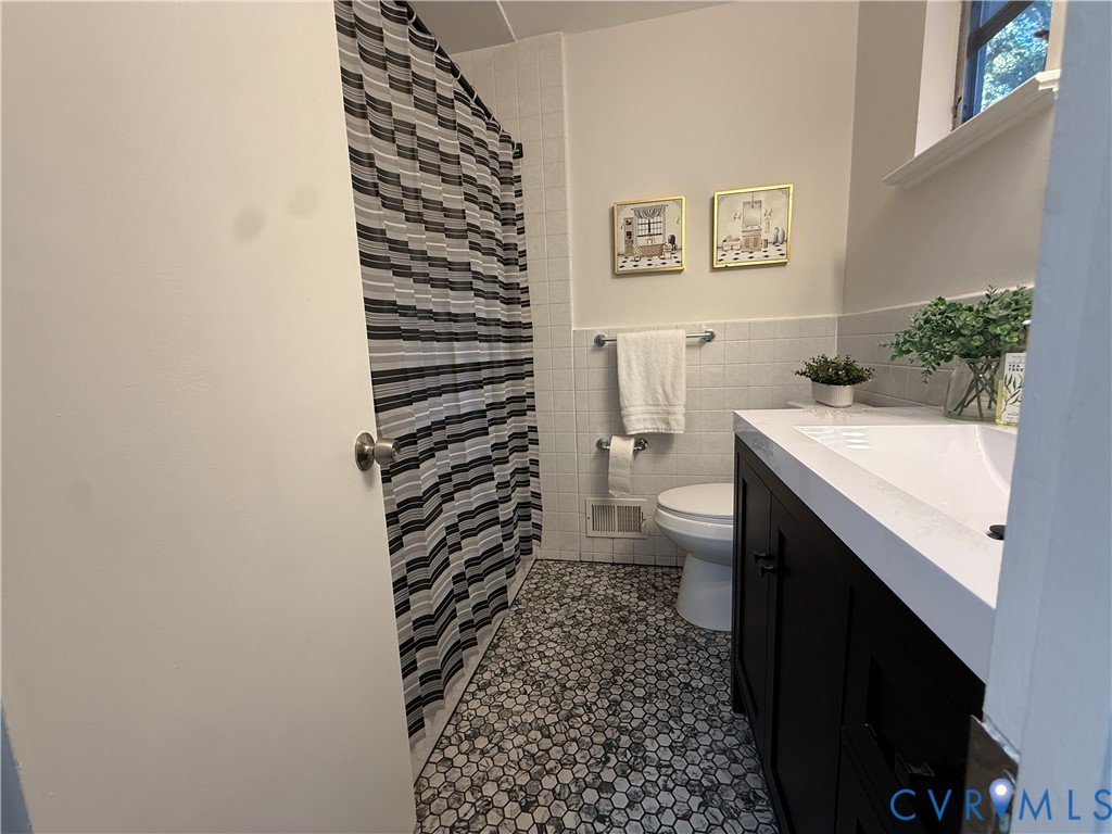 Bathroom featuring a dark-finish vanity with a rectangular sink, white countertop, hexagon tile flooring, and wall-tiled tub enclosure