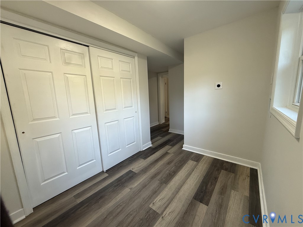 Neutral-toned walls paired with wood-finish flooring, featuring a dual-panel sliding closet and a window with white trim