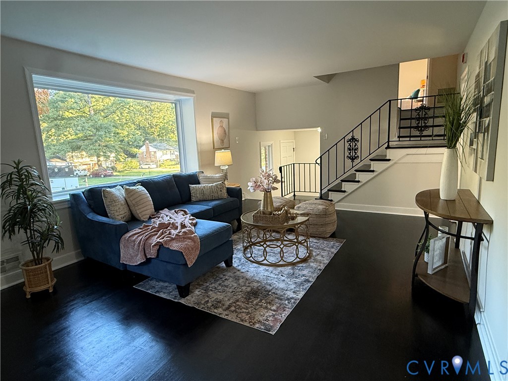 Large picture window, dark hardwood flooring, and open staircase featuring decorative wrought iron railings
