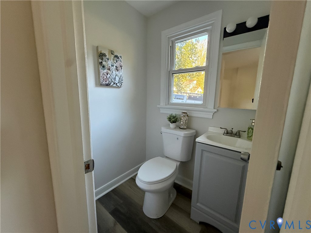 Neutral-toned interior featuring wood-finish flooring, a vanity with an integrated sink and chrome dual-handle faucet, a window with decorative molding, and a two-piece toilet