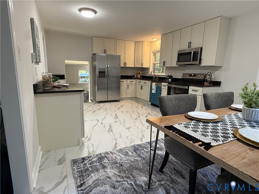Kitchen featuring white cabinetry, dark countertops, stainless steel appliances, and large-format tile flooring