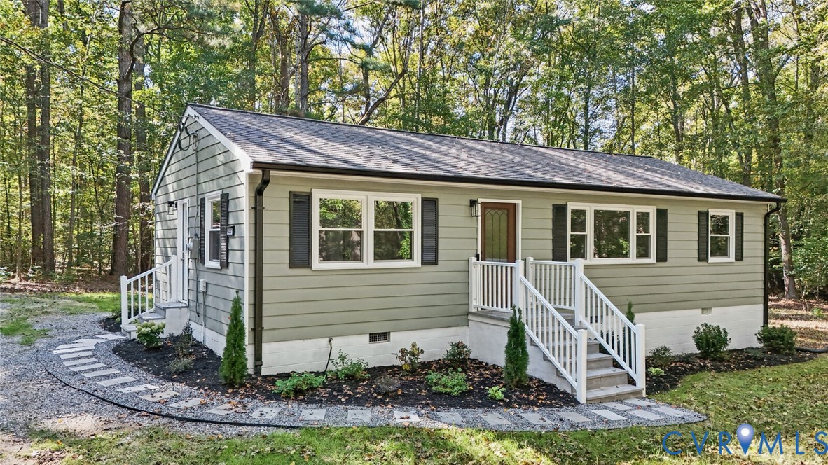 Exterior featuring horizontal lap siding, white-railed entry steps, shuttered windows, and a stone paver walkway surrounded by mature trees