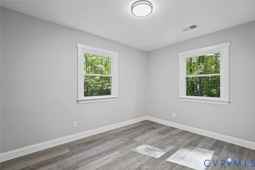 Room featuring wood-finish flooring, neutral walls, two windows with white trim, and a ceiling-mounted light fixture