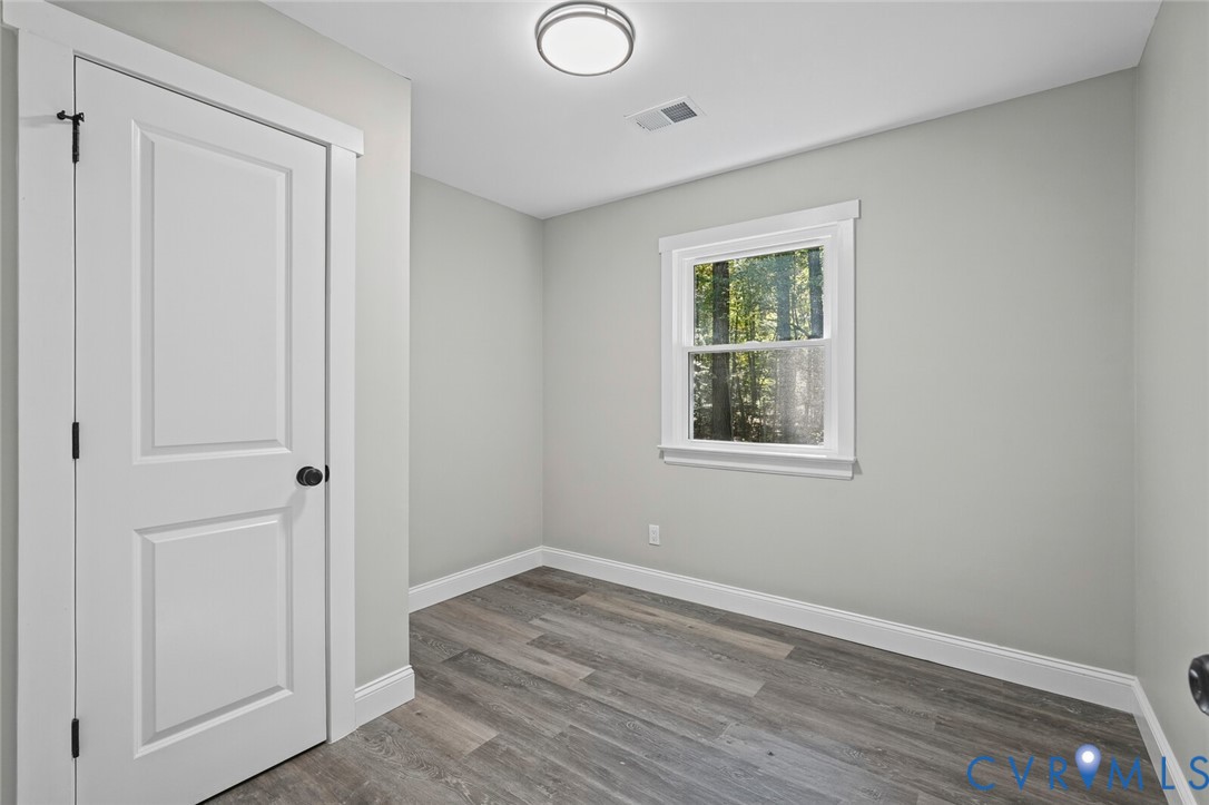 Room interior featuring wood-finish flooring, crisp neutral wall paint, a single-hung window with casing, and a paneled interior door with matte black hardware