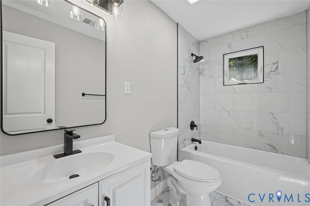 Bathroom featuring white vanity cabinetry, rectangular mirror with black frame, matte black hardware, and tub surround finished with white tile