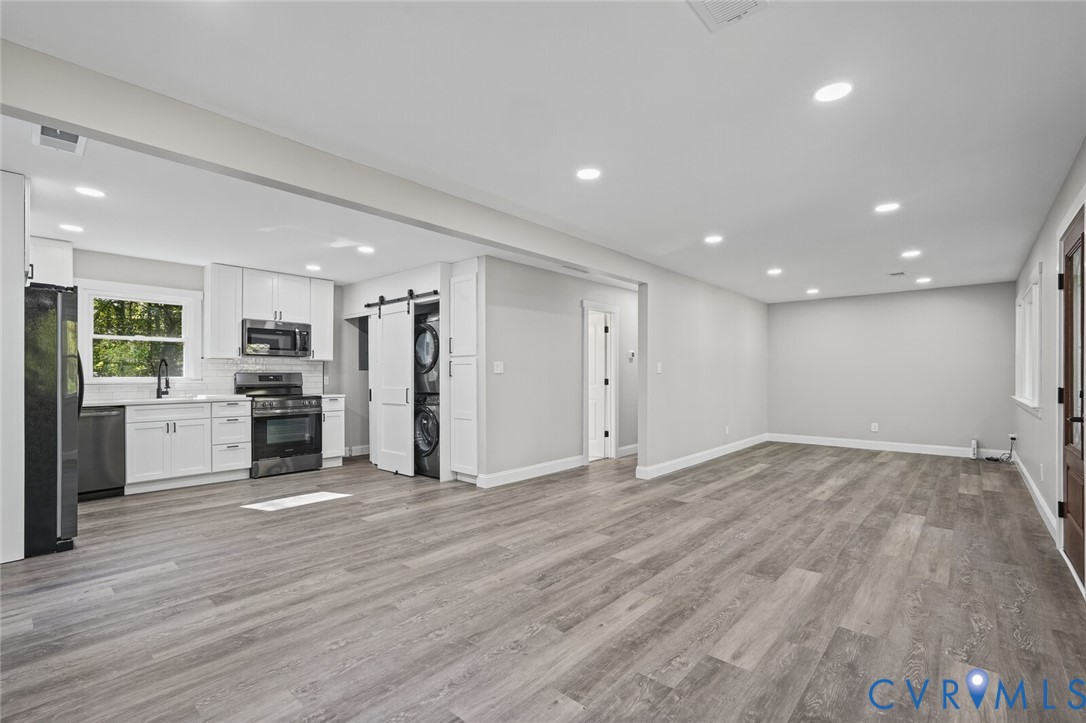 Kitchen area featuring white shaker-style cabinetry, stainless steel appliances, wood-finish flooring, recessed lighting, and a sliding barn door concealing a laundry station