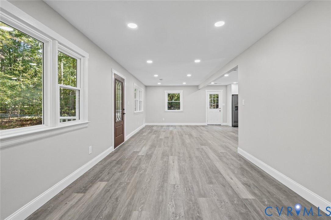 Open-concept interior featuring wood-finish flooring, recessed lighting, multiple multi-pane windows, and a dark-toned exterior door with decorative glass inlay
