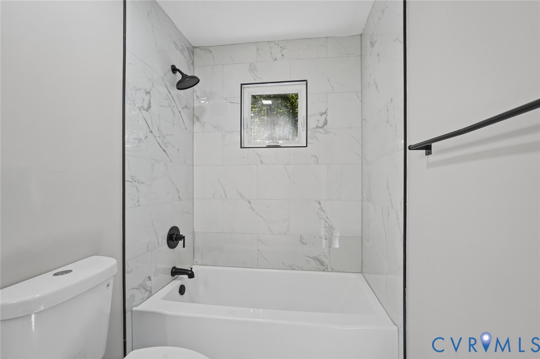 Bathtub and shower surround featuring large-format white tile with grey veining, matte black fixtures, and a square window