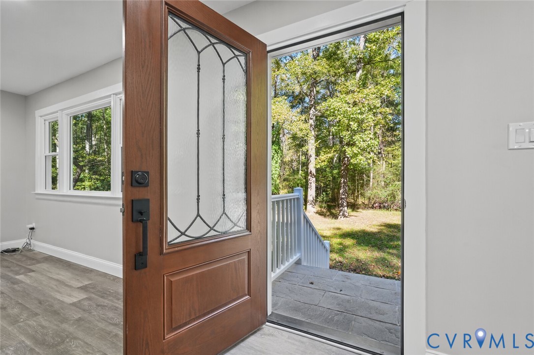 Solid wood-finish entry door with decorative glass insert, black hardware, wood-finish flooring, and natural stone exterior porch