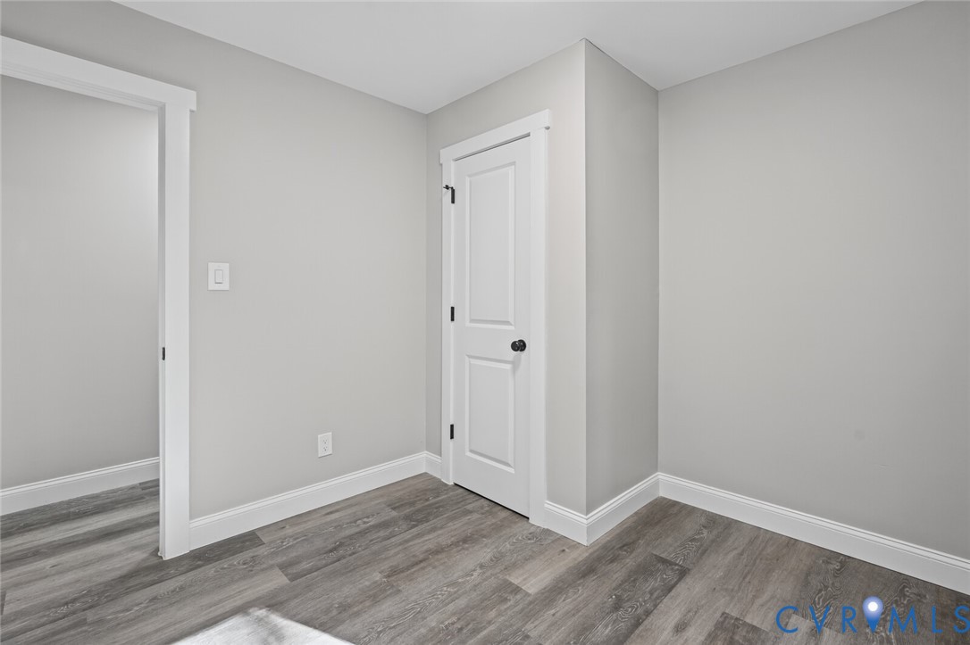Neutral interior space featuring wood-finish flooring, crisp white casing, and a two-panel interior door with matte black hardware