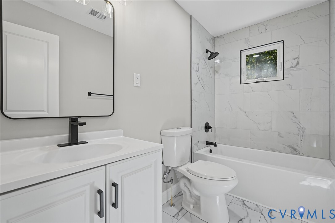 Bathroom featuring a white vanity cabinet, rectangular mirror with a black frame, matte black hardware, and a tub enclosure with large-format light-toned patterned wall tiling