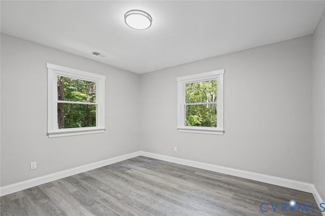Neutral interior featuring wood-finish flooring, two double-hung windows with white casing, and a flush-mount overhead light fixture