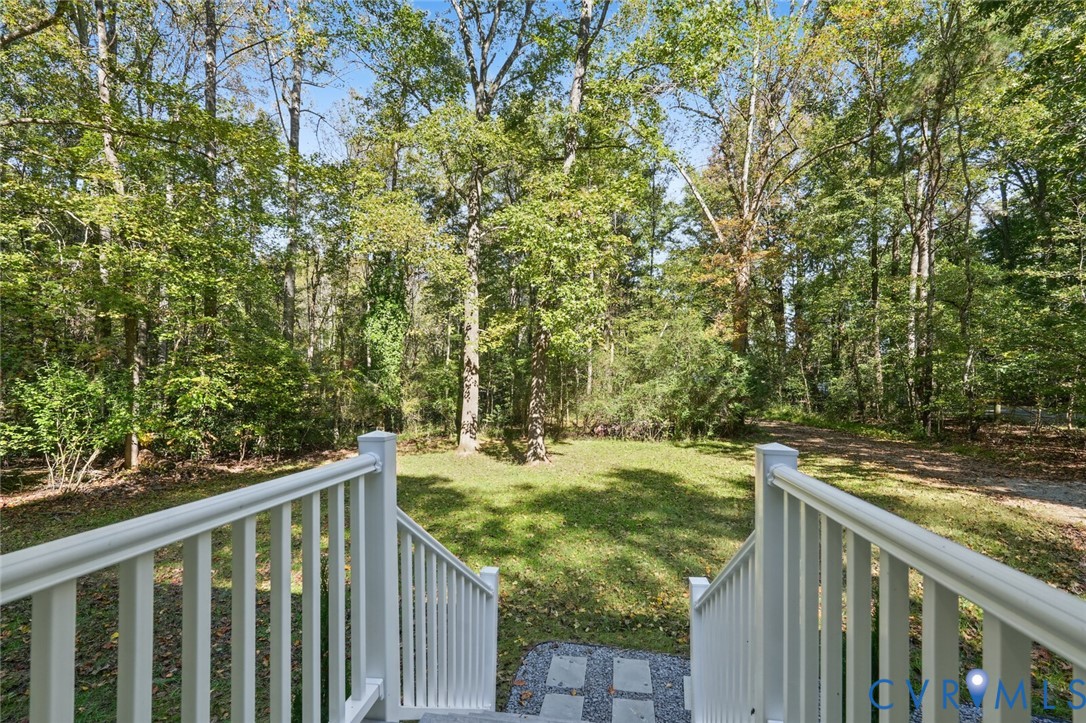 White balustrade staircase, expansive grass lawn, mature tree canopy, and stone paver walkway