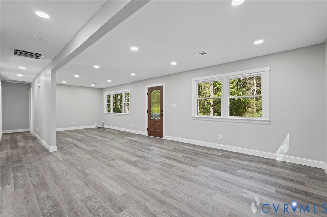 Open interior space featuring wood-finish flooring, recessed lighting, multi-pane windows, and a wood entry door with glass insert