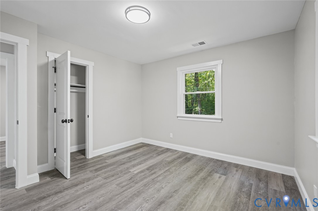 Neutral interior room featuring wood-finish flooring, crisp white trim, a single-hung window, and a built-in closet with a panel door