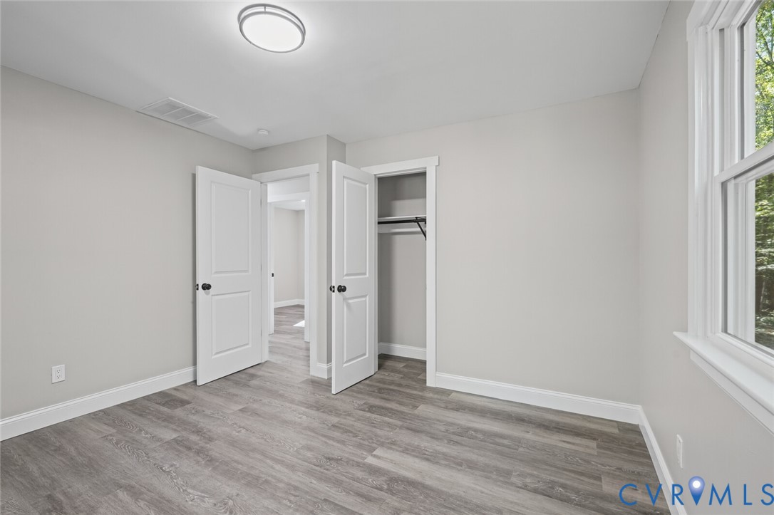 Neutral-toned interior featuring wood-finish flooring, two-panel interior doors with matte black hardware, and an integrated closet with shelving