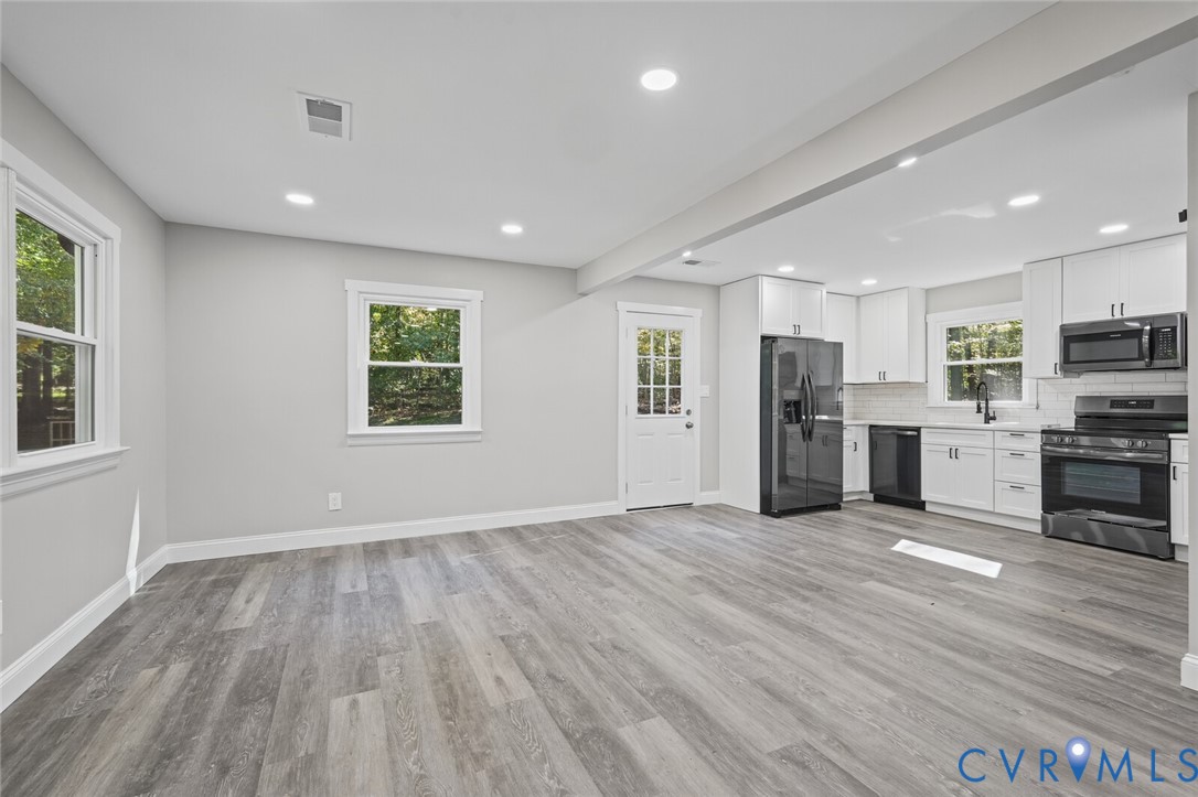 Open-concept area featuring wood-finish flooring, recessed lighting, white shaker-style cabinetry, matte black hardware, and an integrated appliance suite