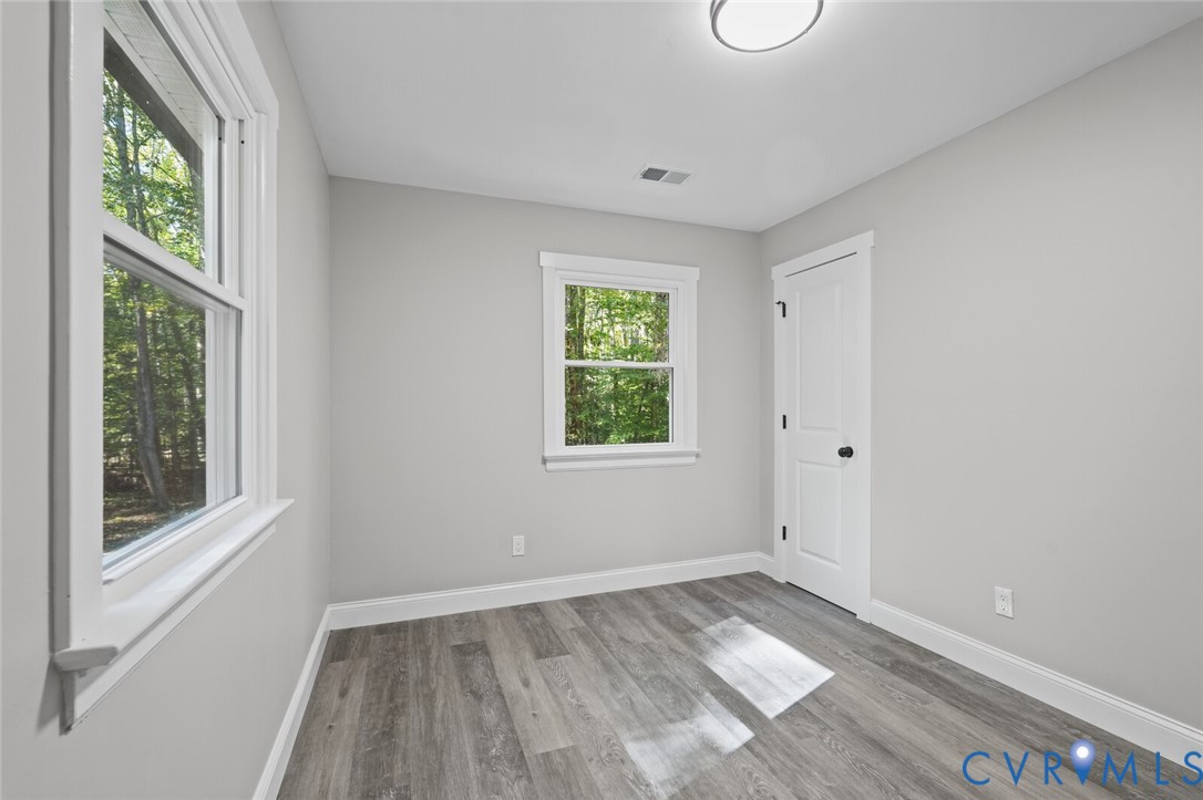 Neutral-toned interior featuring wood-finish flooring, two double-hung windows with white trim, and a paneled interior door with matte black hardware