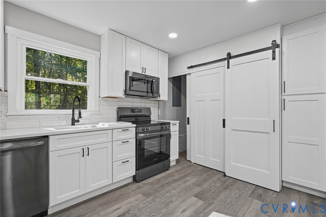 Kitchen featuring white shaker-style cabinetry, quartz countertops, subway tile backsplash, stainless steel appliances, and a sliding barn door