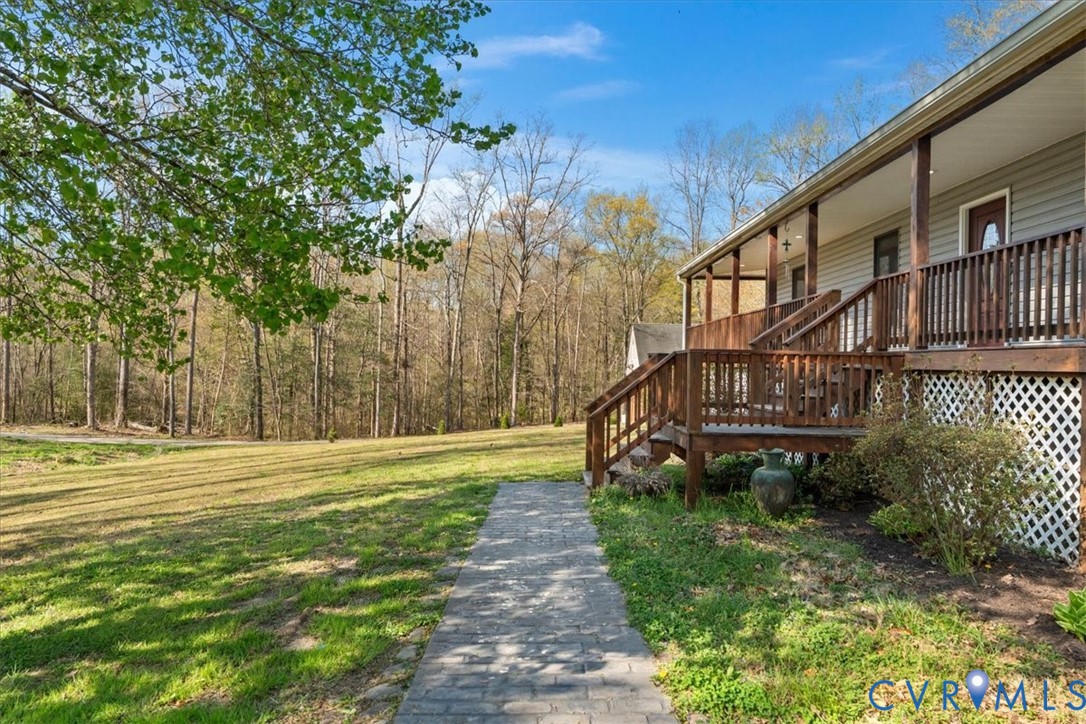 Expansive lawn featuring mature trees, a paver walkway, and a raised wooden deck with lattice skirting