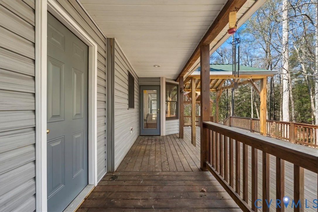Covered wooden deck featuring horizontal siding, wooden balustrades, a built-in gazebo structure, and exterior doors