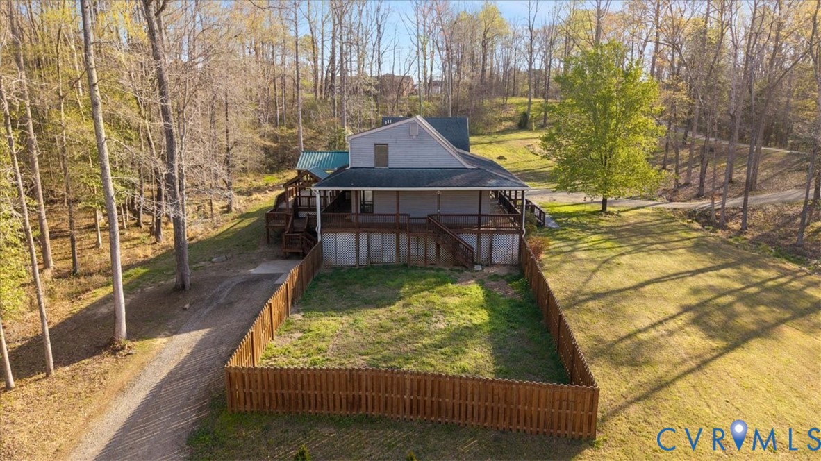 Multi-level exterior featuring a covered wrap-around deck, fenced yard area, and a gravel driveway, situated on a wooded lot