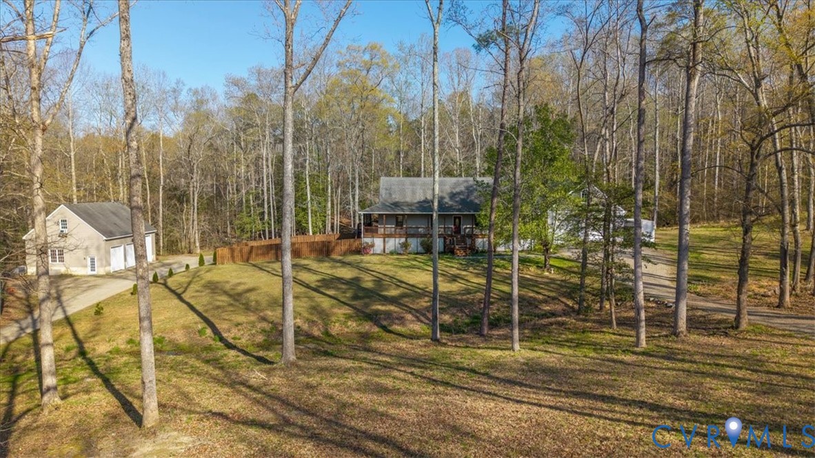 Residential property featuring a sprawling lot with mature trees, a detached multi-car garage, and a wrap-around porch