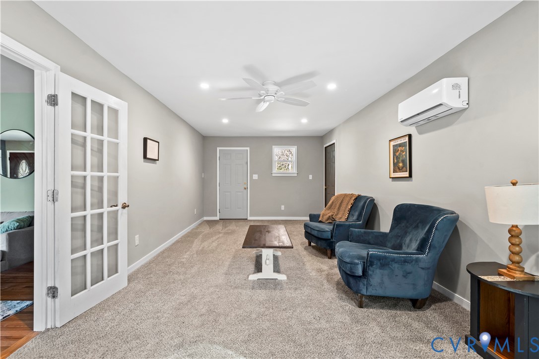Neutral-toned interior space featuring a ceiling fan, wall-mounted split-system air conditioning unit, and a white French door with glass panes Neutral-toned interior space featuring a ceiling fan, wall-mounted split-system air conditioning unit, and a white French door with glass panes